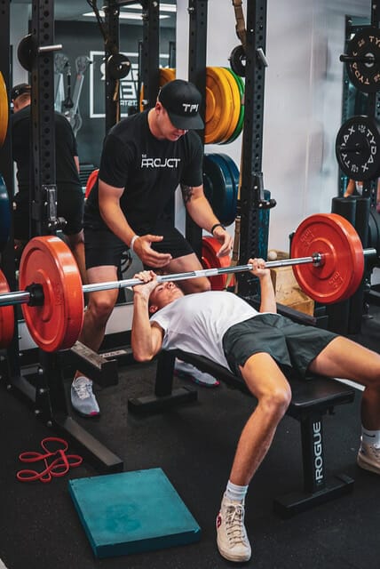 Man lifting weights on bench with coach at People on Group Training at PROJCT Athletics